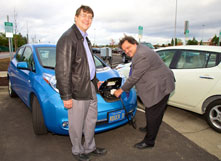 two men charging an electric vehicle at a charging station.